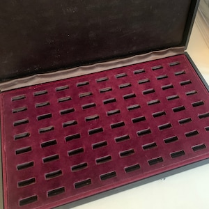May include: A black velvet-lined coin collection box with 60 individual compartments for storing coins.