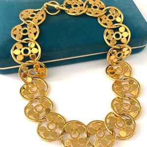 Op de afbeelding: Een gouden ketting met een ketting van in elkaar grijpende cirkels. Elke cirkel heeft een patroon van kleinere cirkels.