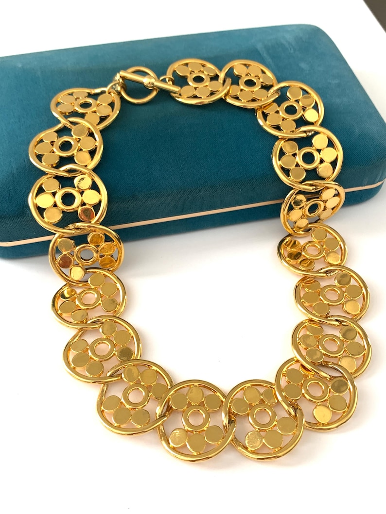 Op de afbeelding: Een gouden ketting met een ketting van in elkaar grijpende cirkels. Elke cirkel heeft een patroon van kleinere cirkels.