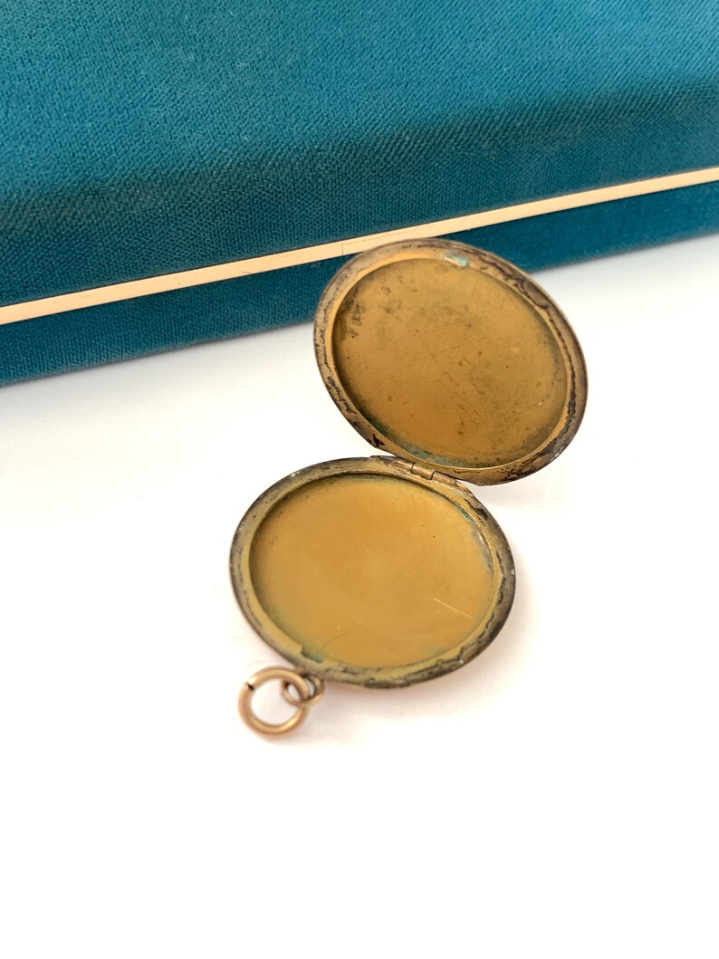 Puede incluir: Un medall&oacute;n de oro con una tapa con bisagras, abierto para revelar un interior vac&iacute;o. El medall&oacute;n tiene un peque&ntilde;o bucle para sujetar una cadena.