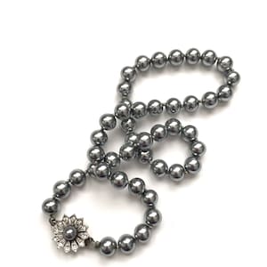 May include: A silver pearl necklace with a silver flower clasp. The pearls are round and have a slight shimmer.