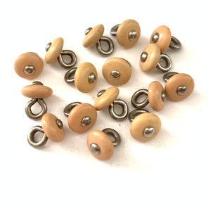 May include: A group of 14 beige plastic buttons with a silver loop and a silver dot in the center.