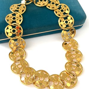 Op de afbeelding: Een gouden ketting met een geometrisch ontwerp. De ketting is gemaakt van in elkaar grijpende cirkels met een bloemmotief.