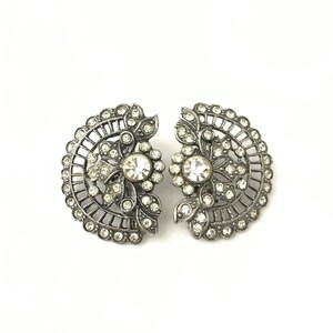 May include: A pair of silver tone clip-on earrings with a floral design and clear rhinestones.