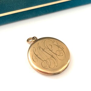 Puede incluir: Medall&oacute;n de oro con un monograma grabado. El medall&oacute;n es redondo y tiene una tapa con bisagras. El monograma est&aacute; en una escritura cursiva.