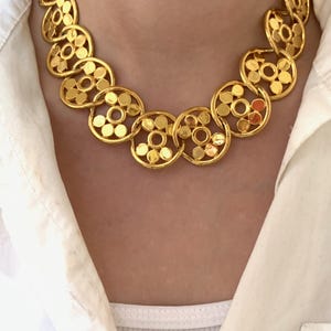 Op de afbeelding: Een gouden ketting met een ketting gemaakt van in elkaar grijpende cirkels. Elke cirkel heeft een patroon van kleinere cirkels.