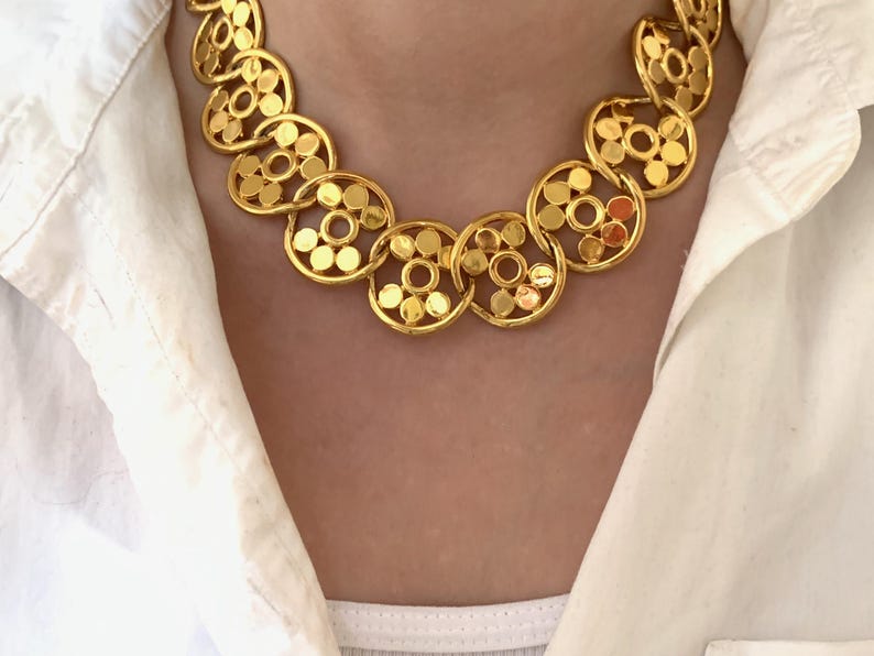 Op de afbeelding: Een gouden ketting met een ketting gemaakt van in elkaar grijpende cirkels. Elke cirkel heeft een patroon van kleinere cirkels.