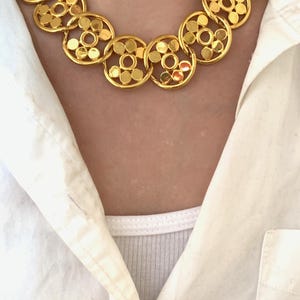 Op de afbeelding: Een gouden ketting met een ketting van gekoppelde cirkels. Elke cirkel heeft een patroon van kleinere cirkels.