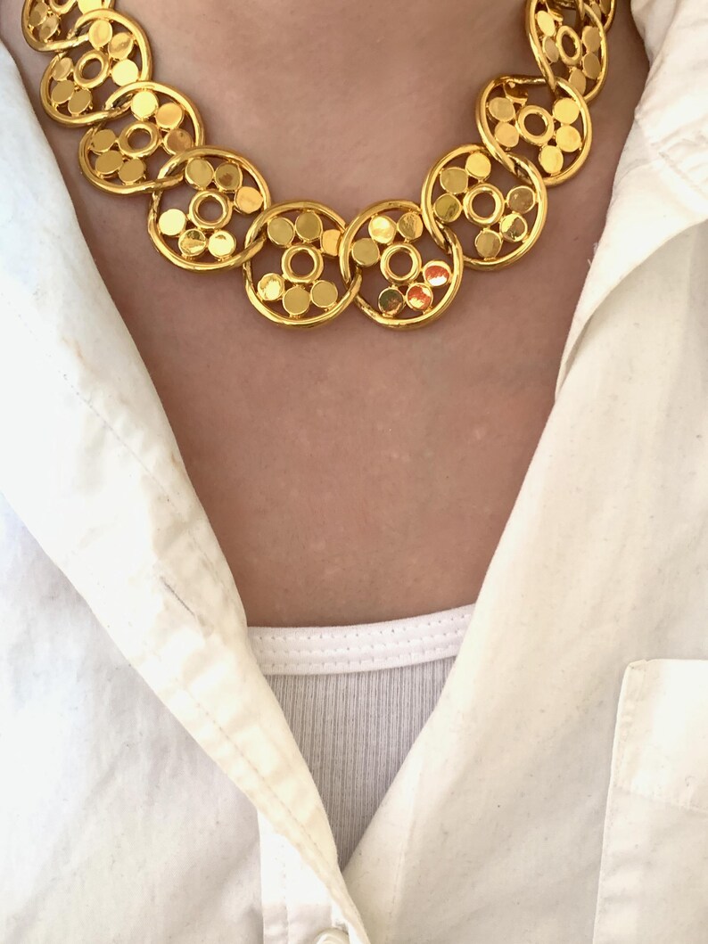 Op de afbeelding: Een gouden ketting met een ketting van gekoppelde cirkels. Elke cirkel heeft een patroon van kleinere cirkels.