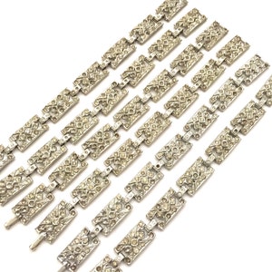 May include: A set of eight silver tone bracelets with a geometric design. Each bracelet is made of linked rectangular pieces that are covered in clear rhinestones.