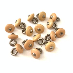 May include: A group of 12 beige plastic buttons with a silver loop and a silver dot on top.