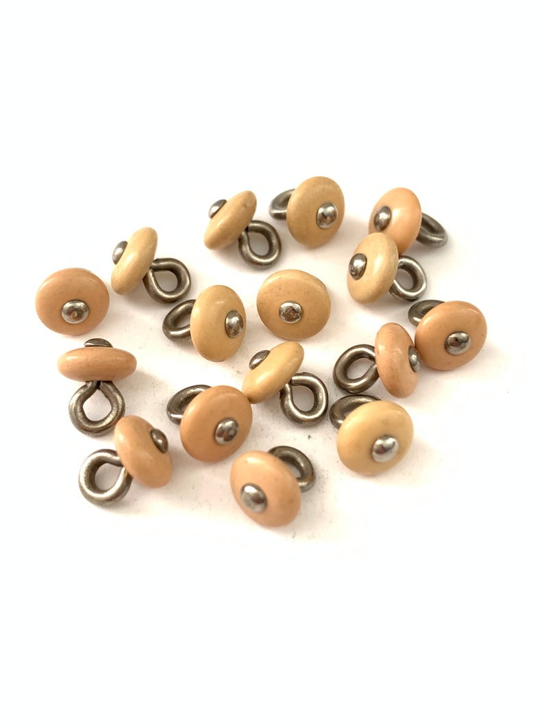 May include: A group of 12 beige plastic buttons with a silver loop and a silver dot on top.