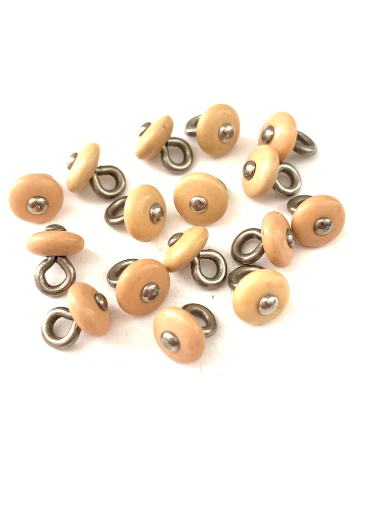 May include: A group of 15 beige plastic buttons with a silver loop and a silver dot in the center.