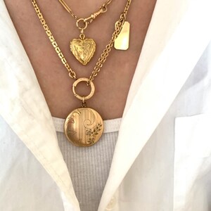 Puede incluir: Tres collares de oro con diferentes colgantes. El collar superior tiene un peque&ntilde;o medall&oacute;n en forma de coraz&oacute;n, el collar del medio tiene una etiqueta rectangular y el collar inferior tiene un medall&oacute;n redondo con dise&ntilde;os florales.