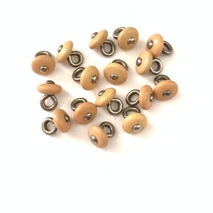 May include: A group of 15 beige plastic buttons with a silver loop and a silver dot in the center.