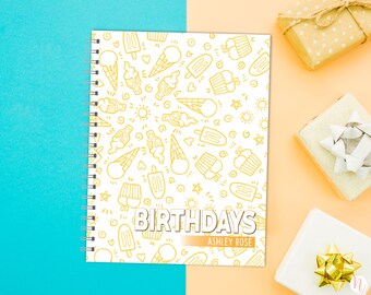 May include: A white spiral bound notebook with a yellow ice cream cone and popsicle pattern. The text "BIRTHDAYS" is printed in yellow on the cover with the name "ASHLEY ROSE" printed below.