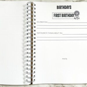 K&ouml;nnte beinhalten: Eine wei&szlig;e Seite aus einem Erinnerungsbuch zum ersten Geburtstag eines Babys mit dem Text "BIRTHDAYS" und "FIRST BIRTHDAY" in Schwarz. Die Seite hat Zeilen zum Schreiben &uuml;ber die Feier und die Lieblingsdinge des Babys. Es gibt Platz f&uuml;r ein Foto.