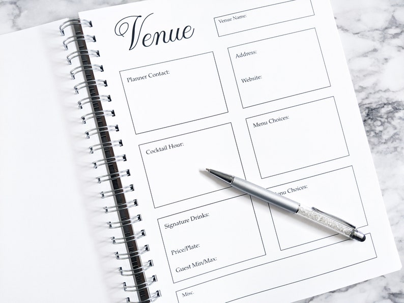 May include: A white spiral bound notebook with a black title "Venue" and sections for planning a wedding or event. The notebook has sections for venue name, address, website, planner contact, cocktail hour, menu choices, signature drinks, price per plate, guest minimum and maximum, and miscellaneous notes.