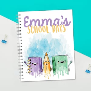 May include: A white spiral bound notebook with a watercolor background and the text "Emma's School Days". The cover features a purple notebook, a yellow pencil, and a green book with cartoon faces.