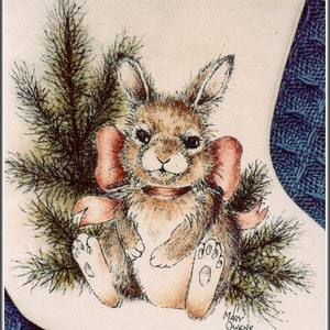 May include: A hand-painted Christmas stocking featuring a brown bunny with a red bow sitting in a bed of green pine needles. The stocking is signed "Mary Owens".