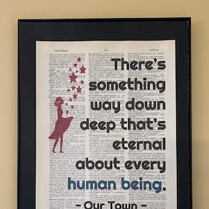 May include: A framed print with a vintage dictionary page background featuring a red silhouette of a girl with stars. The text on the page reads "There's something way down deep that's eternal about every human being. - Our Town"