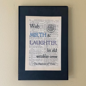 May include: A framed print of a page from a book with the text "KING HENRY VI-SECOND PART" and the words "With MIRTH & LAUGHTER let old wrinkles come" highlighted in blue and purple. The text "The Merchant of Venice" is also visible at the bottom of the page.