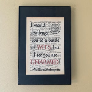 May include: A framed print of a vintage book page with a quote from William Shakespeare's King Henry VIII. The quote reads "I would challenge you to a battle of wits, but I see you are unarmed!" The text is in a black font with red highlights.