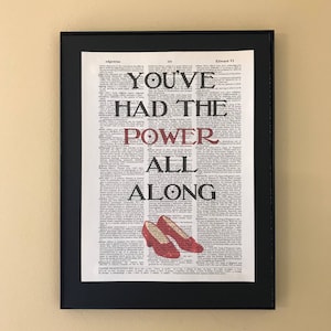 May include: A framed print of a dictionary page with the text "You've had the power all along" in red and black lettering. The text is superimposed over a vintage dictionary page.  The print features a pair of red ruby slippers.