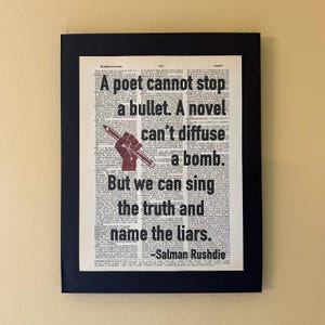 May include: Framed print featuring a quote by Salman Rushdie: "A poet cannot stop a bullet. A novel can't diffuse a bomb. But we can sing the truth and name the liars." The artwork includes a red fist holding a pen.