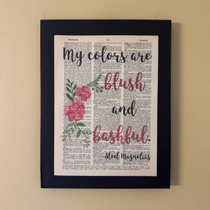 May include: A framed print with a dictionary page background featuring pink flowers and the text "My colours are blush and bashful - Steel Magnolias".