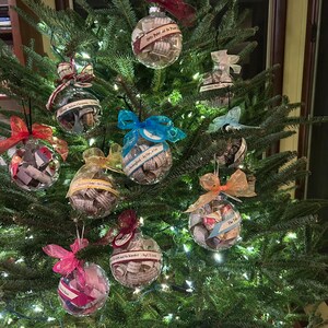 May include: A Christmas tree decorated with clear glass ornaments filled with rolled up pages of books. The ornaments are tied with colorful ribbons and feature titles like "The Wonderful Wizard of Oz" and "Pride and Prejudice".