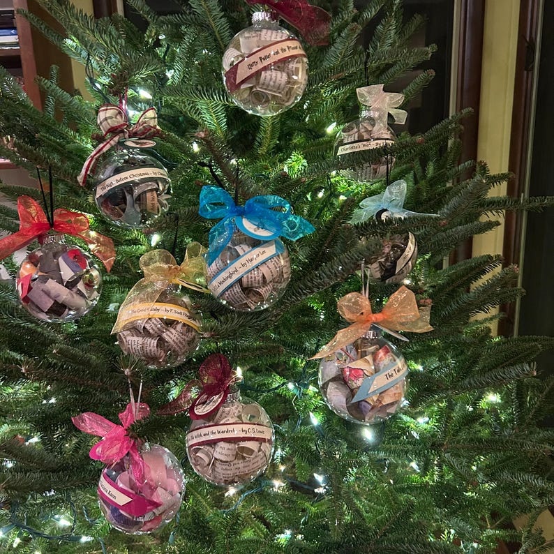 May include: A Christmas tree decorated with clear glass ornaments filled with rolled up pages of books. The ornaments are tied with colorful ribbons and feature titles like "The Wonderful Wizard of Oz" and "Pride and Prejudice".