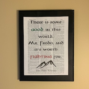 May include: A framed print with a dictionary page background featuring a quote from The Two Towers by J.R.R. Tolkien. The quote reads "There is some good in this world, Mr. Frodo, and it's worth fighting for." The quote is written in a stylized font with green and red accents. The words "The Two Towers" are printed at the bottom of the page.