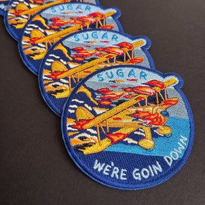May include: Five embroidered patches with a yellow airplane flying over a blue and white sea. The airplane has red flames coming from the engine. The text on the patch reads "Sugar We're Goin Down".