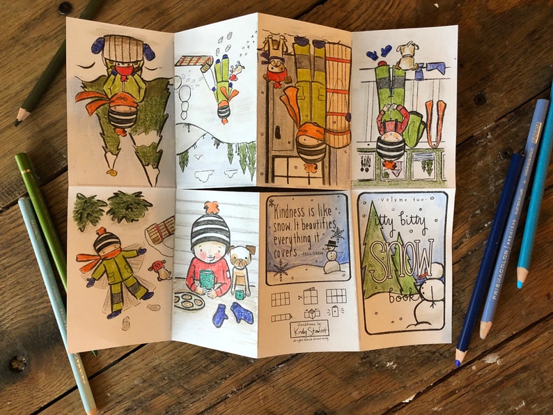 May include: A folded paper booklet with hand-drawn illustrations of winter scenes. The booklet features images of children playing in the snow, a snowman, and the text "Itty Bitty Snow Book". Colored pencils are scattered around the booklet.