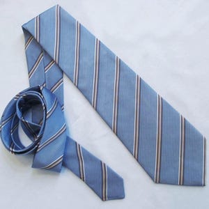 May include: A light blue tie with vertical stripes in white, brown, and light blue. The tie is partially rolled up, showing the striped pattern. The tie is made of a smooth fabric and is suitable for formal or business attire.