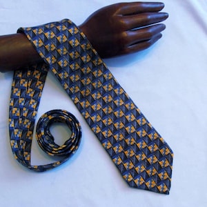 May include: A patterned necktie with a repeating geometric design in navy blue, gold, and gray. The tie is draped over a wooden hand mannequin. The tie is rolled up at the bottom.