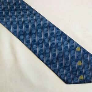 Puede incluir: Una corbata azul con un patr&oacute;n repetitivo de rayas verticales en azul oscuro y finas l&iacute;neas rosa claro. La parte inferior de la corbata muestra tres peque&ntilde;os emblemas bordados de color dorado dispuestos en una l&iacute;nea vertical cerca del borde.