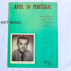 May include: Sheet music titled "April in Portugal" with a teal background and gold lettering. The cover features a portrait of a man in a military-style uniform. Lyrics by Jimmy Kennedy, French words by Jacques Larue, original lyrics by José Galhardo, and music by Raul Ferrão.