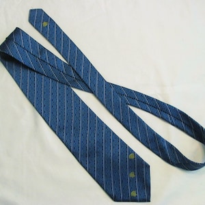 Puede incluir: Una corbata azul con un patr&oacute;n de finas l&iacute;neas blancas verticales y onduladas. La corbata incluye peque&ntilde;os motivos bordados en forma de hoja verde situados cerca del extremo puntiagudo y a lo largo de la secci&oacute;n estrecha del accesorio.
