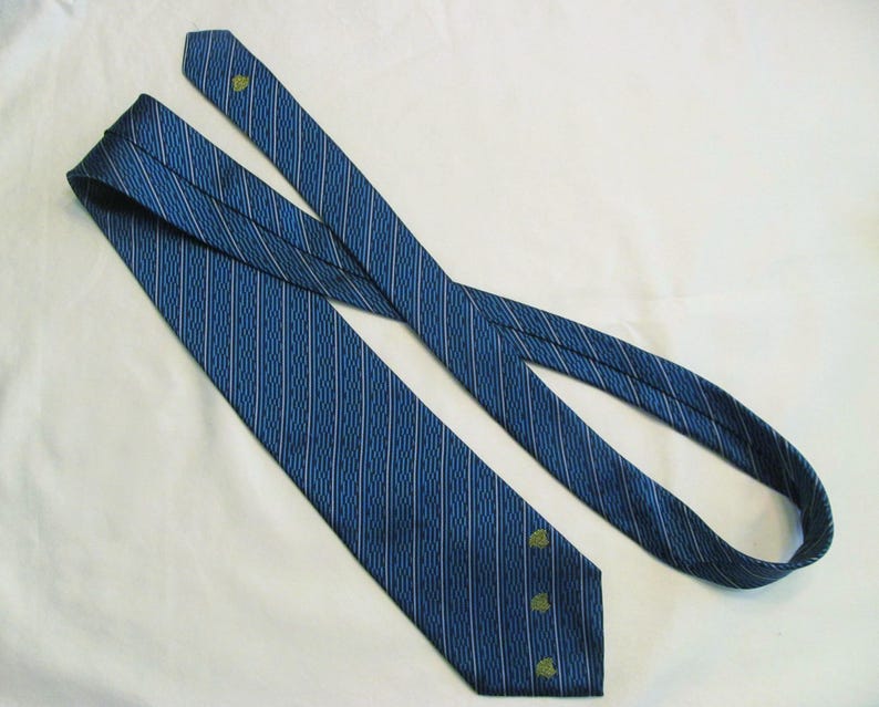 Puede incluir: Una corbata azul con un patr&oacute;n de finas l&iacute;neas blancas verticales y onduladas. La corbata incluye peque&ntilde;os motivos bordados en forma de hoja verde situados cerca del extremo puntiagudo y a lo largo de la secci&oacute;n estrecha del accesorio.