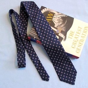 May include: A navy blue tie with a repeating pattern of small pink circles. The tie is draped over a book titled "The Greatest Generation" with a photograph of a man and an American flag.