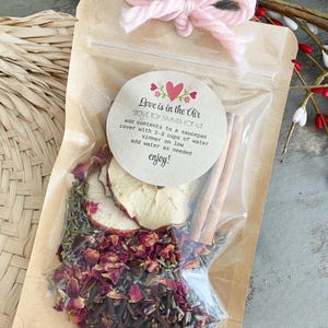 May include: A brown paper bag with a clear plastic window filled with dried fruit, spices, and herbs. The bag has a label that says "Love is in the Air Stove Top Simmer Pot Kit" and instructions for making a simmer pot.