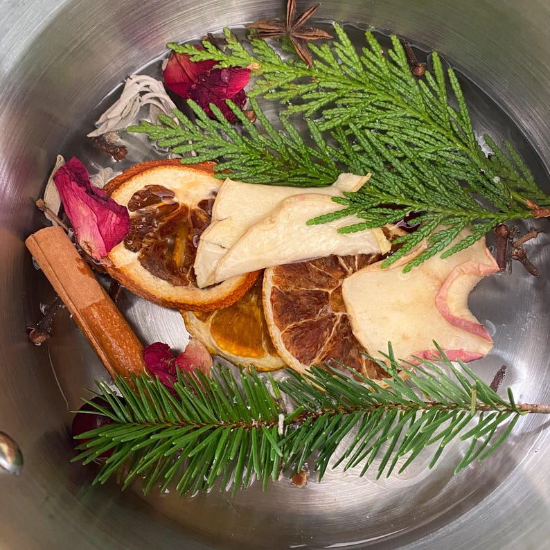 Puede incluir: Una olla llena de fruta seca, especias y ramas de con&iacute;feras para un pote de cocci&oacute;n a fuego lento. Los ingredientes incluyen rodajas de naranja, rodajas de manzana, palitos de canela, an&iacute;s estrellado y ramas de cedro.