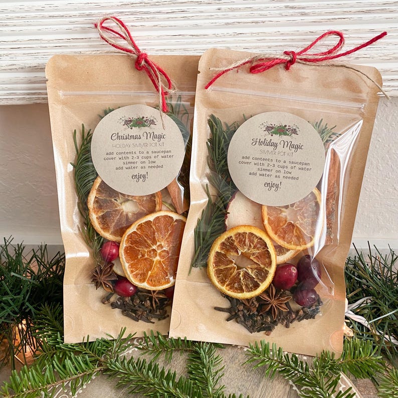 Puede incluir: Dos bolsas de pl&aacute;stico transparente con respaldo de papel marr&oacute;n, cada una contiene un kit de olla de cocci&oacute;n a fuego lento para las fiestas. Las bolsas est&aacute;n atadas con hilo rojo y marr&oacute;n. Los kits incluyen rodajas de naranja secas, palitos de canela, an&iacute;s estrellado, clavos y ar&aacute;ndanos. Las bolsas tienen etiquetas que dicen "Christmas Magic Holiday Simmer Pot Kit" y "Holiday Magic Simmer Pot Kit".