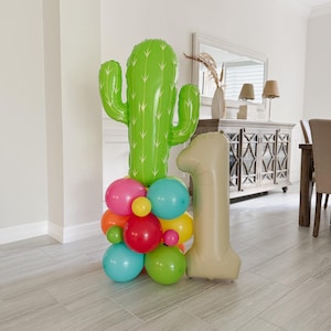 May include: A festive balloon arrangement featuring a large green cactus, a beige number one balloon, and a cluster of colorful balloons in shades of pink, orange, yellow, green, and blue. Perfect for a first birthday celebration.