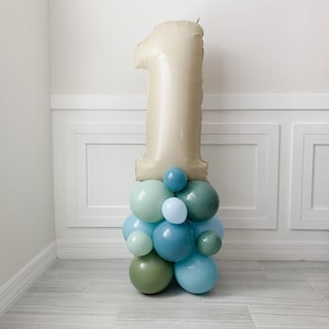 May include: A large beige number one balloon with a cluster of smaller balloons in shades of blue and green at the base.