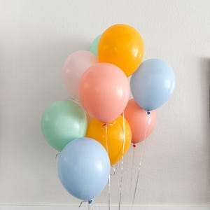 May include: A cluster of colorful balloons in shades of orange, pink, blue, and green. The balloons are tied together with silver ribbons, creating a festive and cheerful display. Perfect for a birthday or celebration.