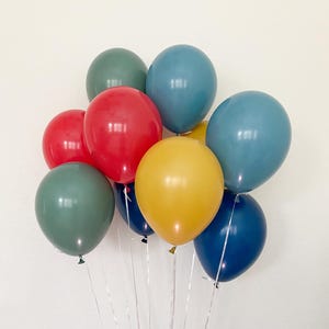 May include: A bunch of balloons in various colors, including red, yellow, green, and blue. The balloons are tied together with white ribbons.
