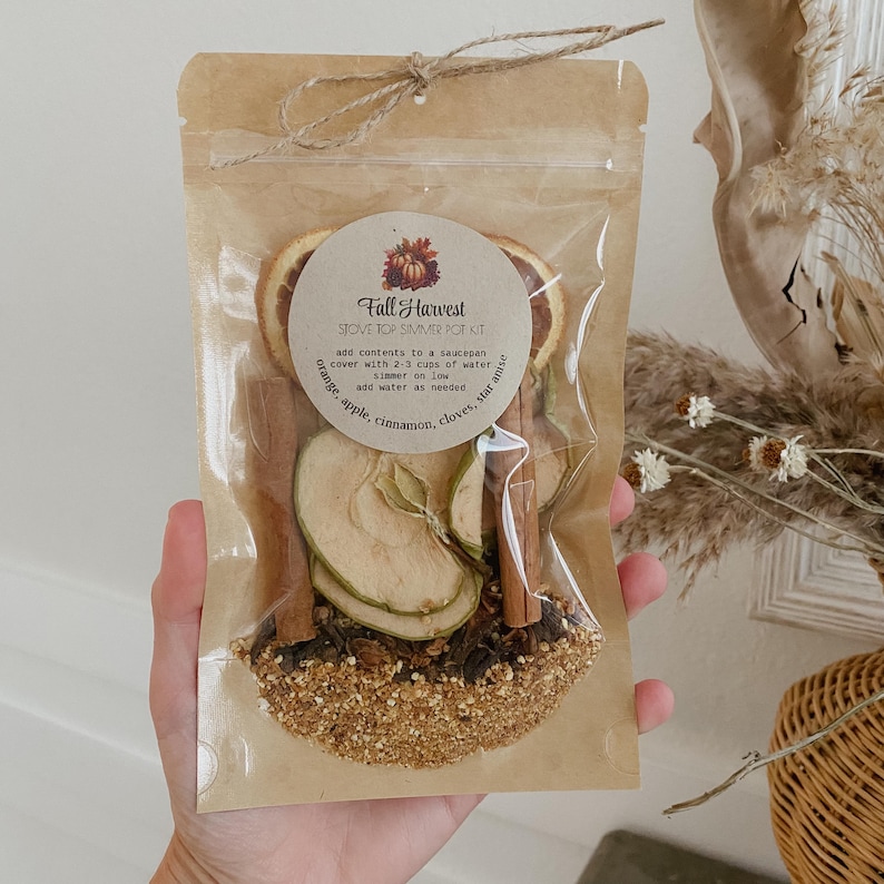 Peut inclure: Un sachet transparent nou&eacute; avec de la ficelle, contenant un kit de pot-pourri pour cuisini&egrave;re Fall Harvest. Le kit comprend des tranches d'orange s&eacute;ch&eacute;es, des tranches de pomme, des b&acirc;tons de cannelle, des clous de girofle et de l'anis &eacute;toil&eacute;. Le sachet a une &eacute;tiquette circulaire avec du texte.
